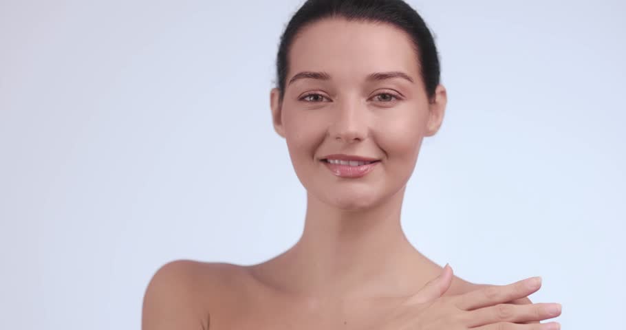 Beautiful Caucasian woman smiles while softly touching her bare shoulder in a peaceful pose. Great for bodycare, skincare, beauty, personal wellness, and feminine elegance visuals.
