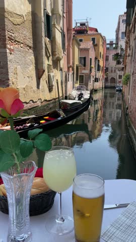Evening Romance with Canal View in Venice: Romantic dinner setting overlooking a tranquil Venetian canal, featuring a plate of spaghetti, a glass of beer, and spritz.