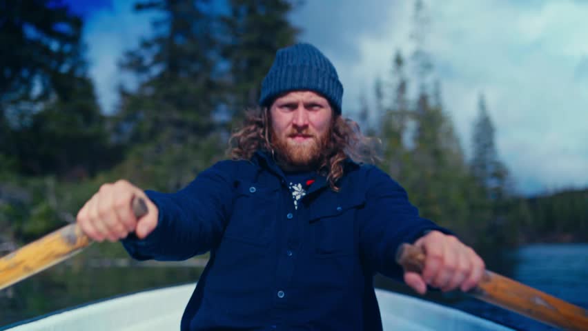 Bearded Man In Beanie Hat Rowing Boat On Lake Reinsjoen In Afjord, Norway. closeup shot