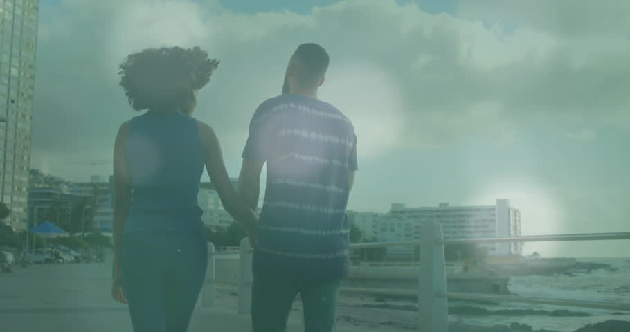 Couple handholding walking seaside glancing at other generating animated bokeh lights for travel. Romantic, leisure, serenity, scenic, lifestyle, modern, connection