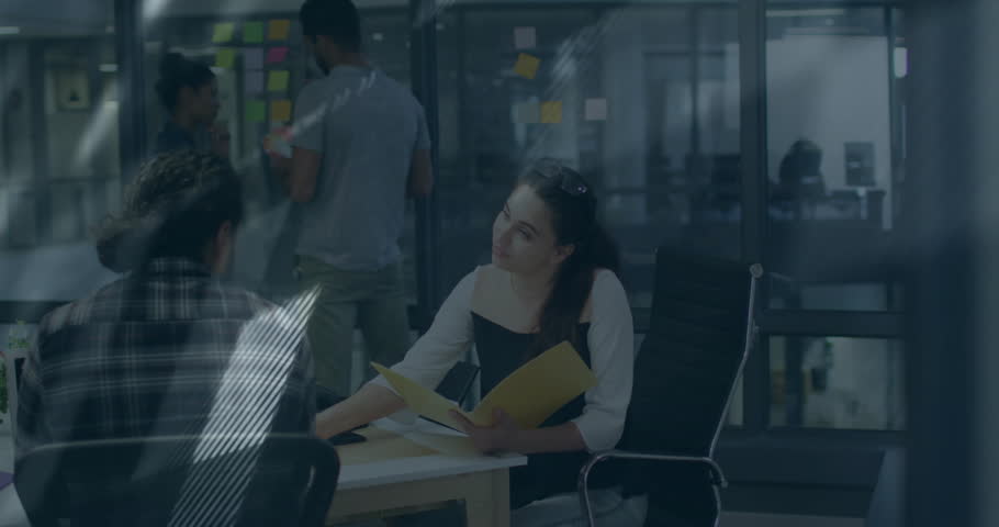 Female professional pointing at monitor and flipping folder as animated graphs showing tech metrics. Collaboration, analytics, teamwork, innovation, data visualization, productivity, corporate