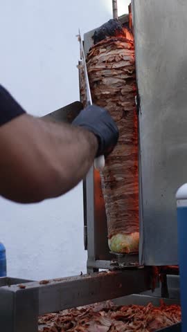 Taquero cutting meat from a grilled beef trompo. Mexican street food.