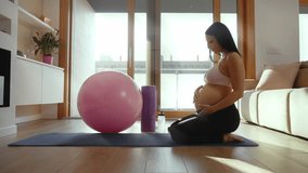 Beautiful pregnant woman practicing pilates exercises with a fitness ball in her living room, promoting health and well-being during pregnancy - Powered by Shutterstock - Get 15% off with code: PIKWIZARD15