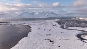 Aerial view over snow-covered plains meeting the icy waters of Borgarfjörður near Borgarnes, with the dramatic peaks of Hafnarfjall, Kessuhorn, and Baula rising in the distance under soft arctic light - Powered by Shutterstock - Get 15% off with code: PIKWIZARD15
