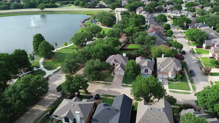 Lush green community Rheudasil Park in Flower Mound, Texas with water fountain, curved boardwalk, walking trails, playground, upscale suburban two-story houses with swimming pools, grassy lawn. USA