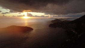 Aerial video of dramatic coastal sunset with sun rays piercing storm clouds, reflecting on calm sea near coastal cliffs and peninsulas in evening light. - Powered by Shutterstock - Get 15% off with code: PIKWIZARD15