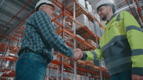 Mature Caucasian male in checkered shirt shaking hands with serious worker wearing bright jacket and helmet. Discussing logistics or closing deal inside large warehouse facility. Partnership concept. - Powered by Shutterstock - Get 15% off with code: PIKWIZARD15