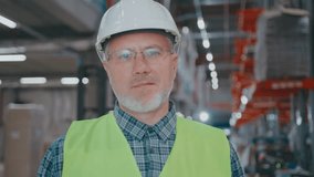 Confident mature Caucasian male with glasses adjusting helmet while standing inside warehouse. Supervising construction safety or reviewing progress during site inspection in organized facility. - Powered by Shutterstock - Get 15% off with code: PIKWIZARD15