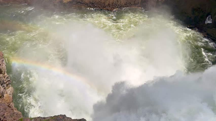 Close up view of the fast-flowing Yellowstone River dropping over the edge of the Upper Falls in Yellowstone National Park with a rainbow in the spray. 