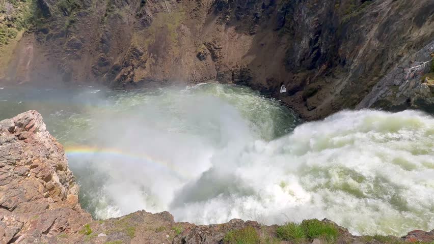 Close up view of the fast-flowing Yellowstone River dropping over the edge of the Upper Falls in Yellowstone National Park with a rainbow in the spray. 