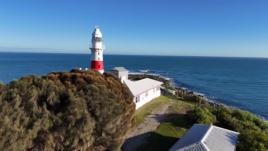 Low Head Lighthouse at sunrise on Tasmania’s northern coast, Australia. A historic red-and-white striped lighthouse overlooking the Bass Strait, set against dramatic skies and rugged coastal scenery.