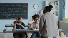 Black female teacher standing in front of young diverse student sitting and listening at their desks during interactive Math lesson in modern classroom - Powered by Shutterstock - Get 15% off with code: PIKWIZARD15