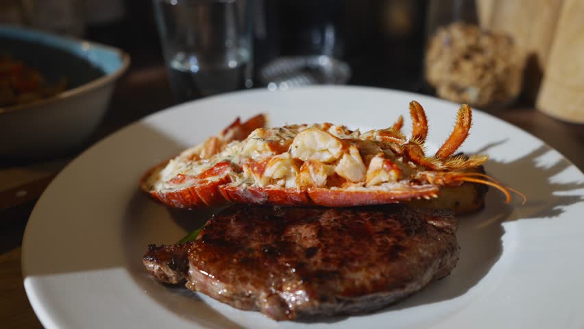 A plate of meat and seafood with a lobster on top. The plate is white and the food is brown