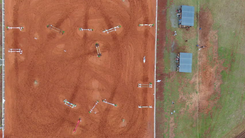 High-altitude drone clip captures rider navigating jumps on rust-colored obstacle course. Ideal for equestrian sports promotions.
