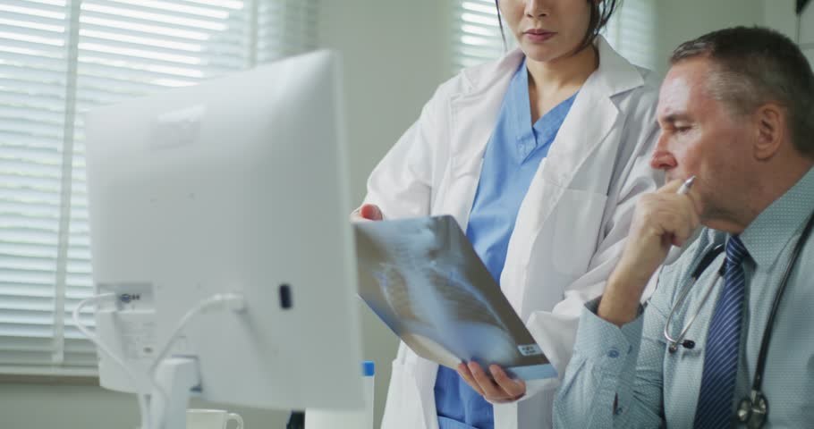 A male doctor and female nurse closely inspect an X-ray image, focusing on diagnosis or patient case review in a clinical setting.