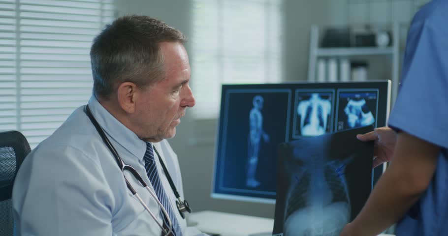 A male doctor and female nurse closely inspect an X-ray image, focusing on diagnosis or patient case review in a clinical setting.