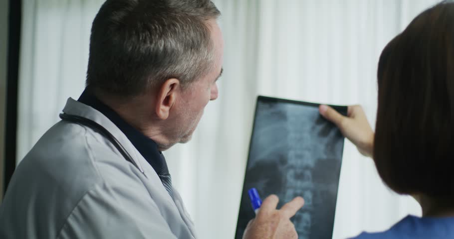 Two medical professionals examine a spinal X-ray together, discussing potential issues or abnormalities for accurate diagnosis and treatment.
