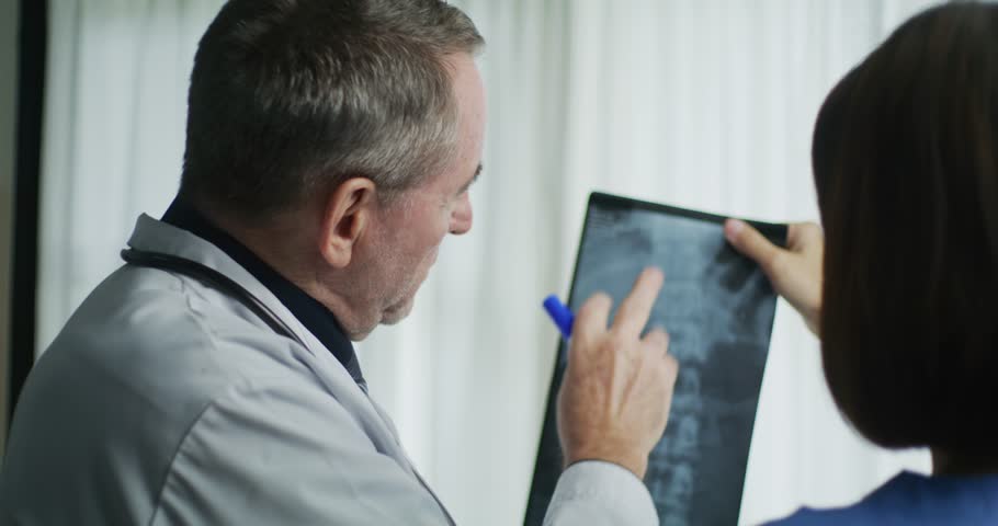 Two medical professionals examine a spinal X-ray together, discussing potential issues or abnormalities for accurate diagnosis and treatment.
