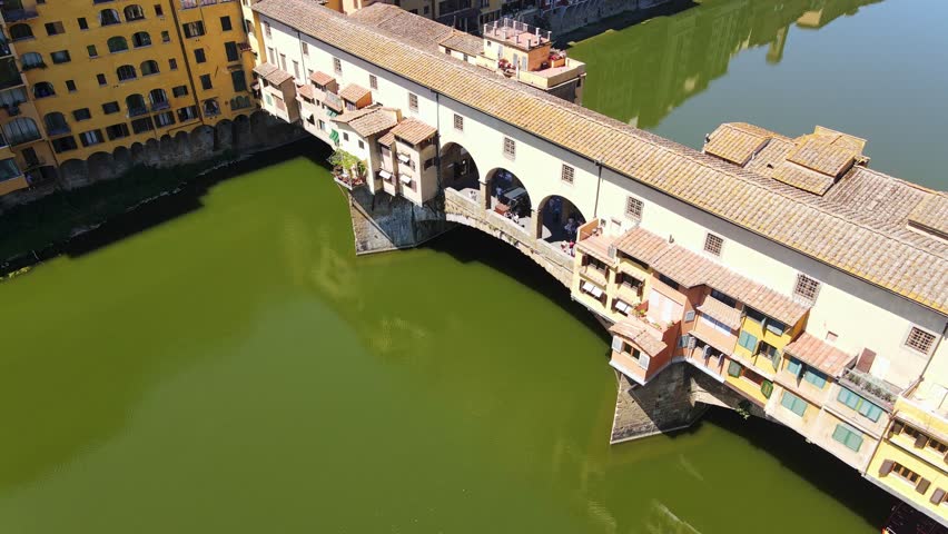 Cinematic aerial of iconic Ponte Vecchio bridge over green Arno river Florence