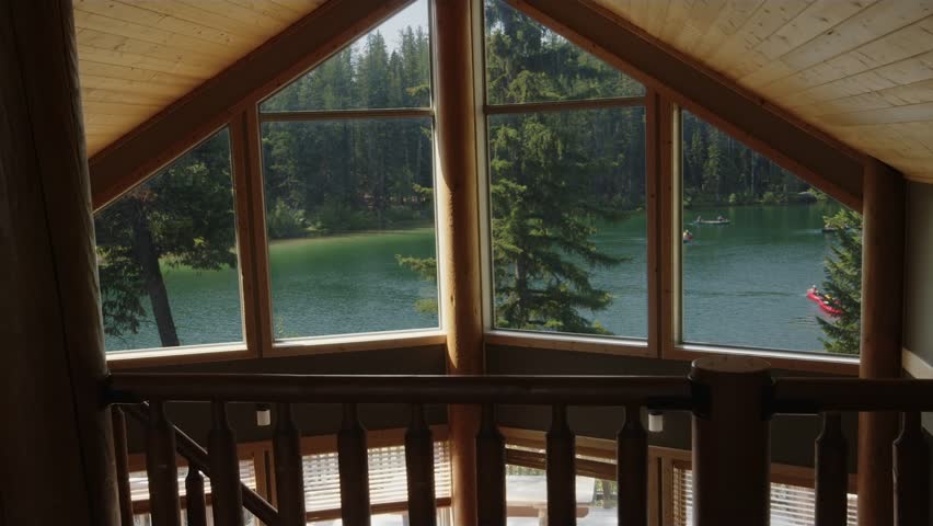 View out picture windows in wood lodge looking over small green lake
