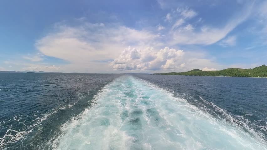 View from the back of a ferry leaving sea trail over calm blue waters under a bright sky in the Philippines.
