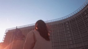 Woman walks under EU flag at dusk. Soft sunlight hits European Commission façade - Powered by Shutterstock - Get 15% off with code: PIKWIZARD15