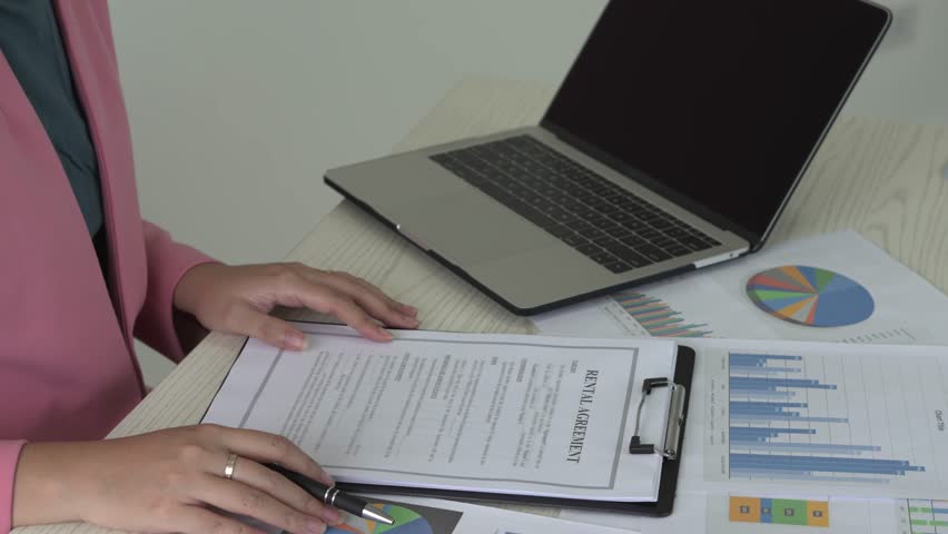 Real estate gent asian woman is reading and checking paper documents, signing the contract to send to her business partner. Concentrated smart ambitious lady is preparing research, remote freelancer.