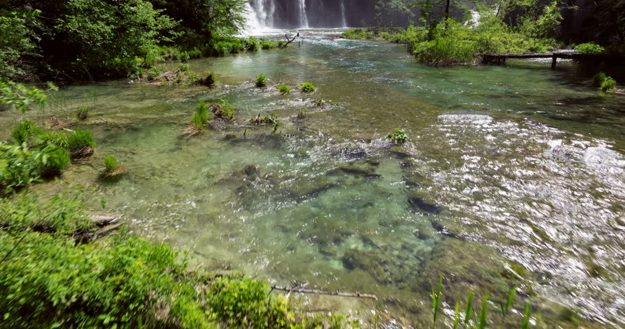 Misty Waterfalls Plunging Over Lush Green Cliffs With Clear Flowing River In Foreground. Plitvice Lakes National Park, Croatia. drone tilt-up reveal