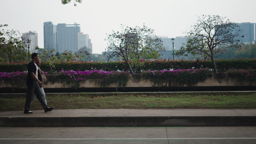 Couple walking together, urban park scene with modern cityscape surrounding relaxed pair