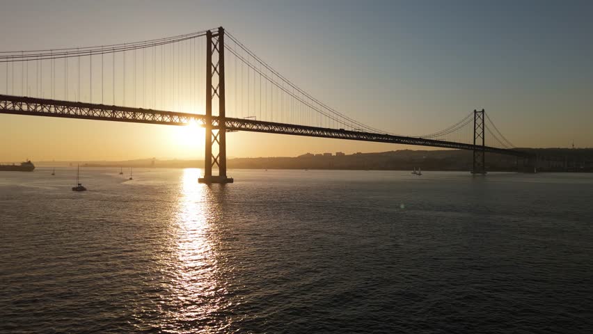 Ponte 25 de Abril Suspension Bridge over Tagus River at Sunset. 25th April Bridge. Portugal. Aerial View. Wide Shot. Drone Moves Forward and Upwards