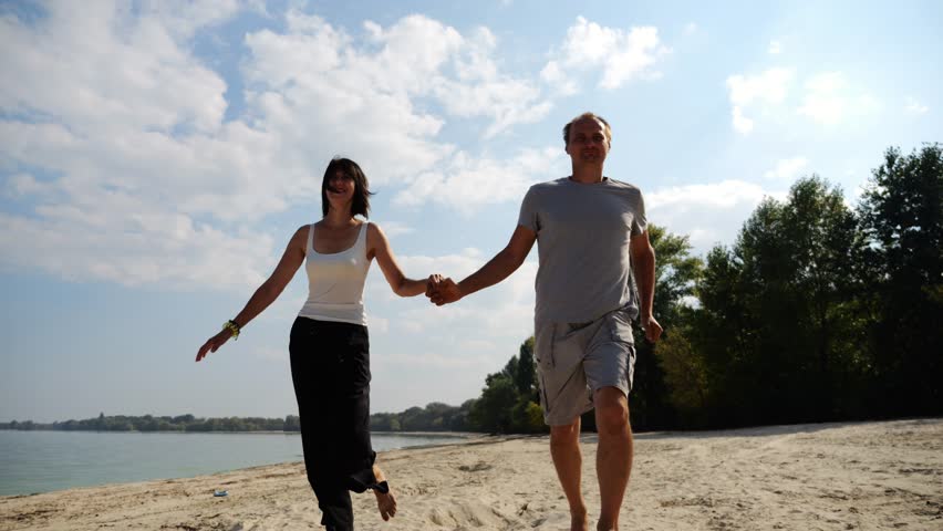 Romantic couple holding hands of each other and jogging at coastal. Happy pair running along seashore at sunny day. Lovers spending time together at resort. Concept of summer vacation or holiday