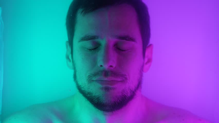 Man Opening Eyes Submerged in Luminous Neon Water