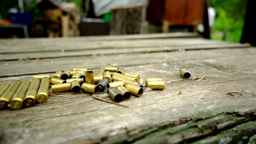 Close up shot of empty bullet shells laying on old wooded table after shooting practice or hunting - slowly moving camera from right to left