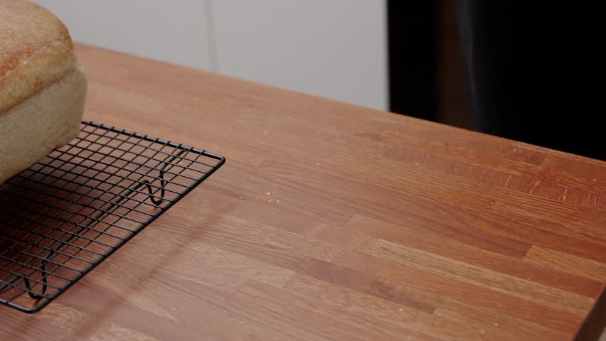 Hands with Oven Mitts Removing Freshly Baked Bread from Loaf Pan on Wooden Kitchen Counter