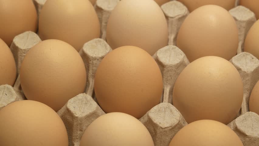 Fresh clean beige chicken eggs in cardboard tray rotates, top view