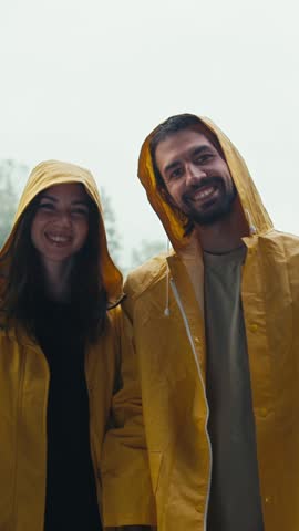 A cheerful couple embraces the joy of a rainy day, clad in bright yellow raincoats, as they share laughter and moments in a picturesque outdoor setting