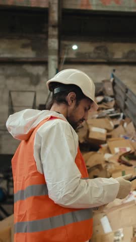 A dedicated worker in safety gear organizes and sorts cardboard boxes at a recycling facility, ensuring efficient waste management while maintaining safety protocols