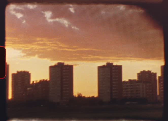 8 mm film - warm sunlight bathing residential buildings in golden hues, casting vibrant orange glow across urban landscape during serene evening twilight with peaceful cityscape atmosphere