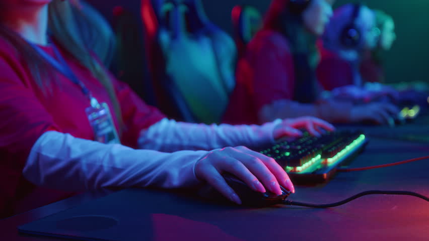 Medium closeup of hands and midsection of team of unrecognizable female gamers sitting in front of computers in cyberclub, playing video game with keyboard and mouse