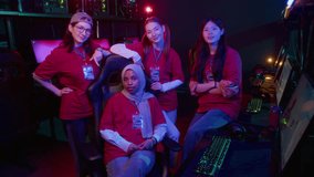 Medium full portrait of cheerful professional diverse female cybersport team posing at computer club, wearing uniform red tshirts, badges, looking at camera, smiling, displaying confidence and success - Powered by Shutterstock - Get 15% off with code: PIKWIZARD15