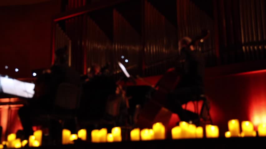 Musicians of an orchestra or ensemble performing surrounded by numerous lit candles. Bokeh, blurred background.
