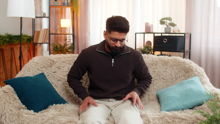 Indian man at home frantically checks pockets and under pillows for lost keys with anxious face. Arabian guy feels stress and confusion, then finally relaxes with relief when he finds them again.