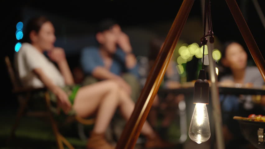 Happy Asian man and woman camping having dinner and talking together in forest mountain at night. People friends enjoy outdoor active lifestyle travel nature, hiking and camping on summer vacation.