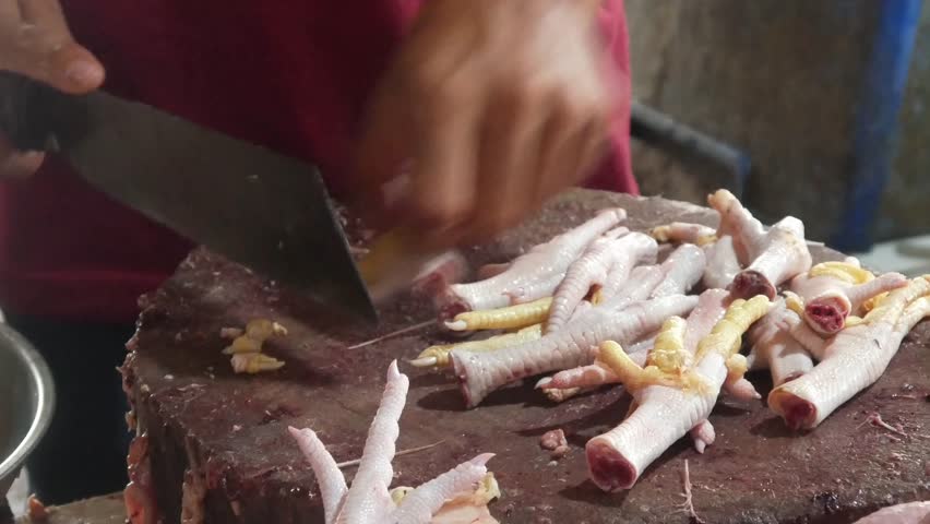 Chicken meat trader cuts chicken feet using a machete on a chopping board