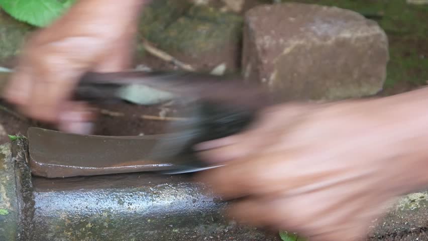 a man's hand sharpening a machete on a sharpening stone