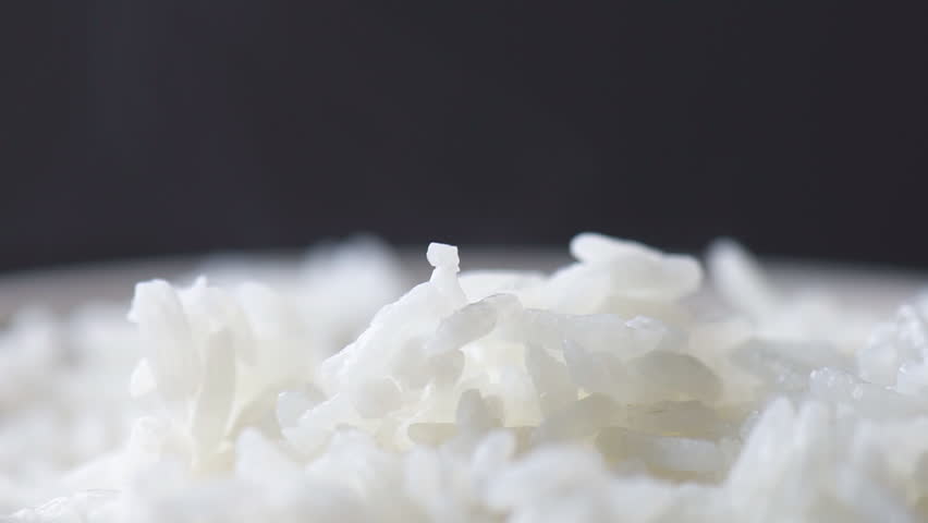 Wooden sticks taking pinch of hot fragrant rice. Macro shot. Bowl of freshly brewed Jasmine rice. Closeup view of long-grain variety of aromatic rice. Healthy eco food. Product of organic farming.