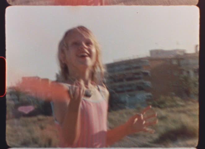 Vintage grainy film capturing young blonde girl playing beach tennis, running with infectious laughter across sandy coastline during sunny summer vacation day - filmed on super 8 mm film