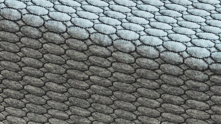 Camera glides upward revealing quilted cells and two-tone stitches on folded mattress