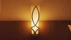 A stylish wall lamp with a warm glow, featuring a unique leaf-like design. The lamp is mounted on a wooden panel, creating a cozy ambiance in a modern interior setting. - Powered by Shutterstock - Get 15% off with code: PIKWIZARD15