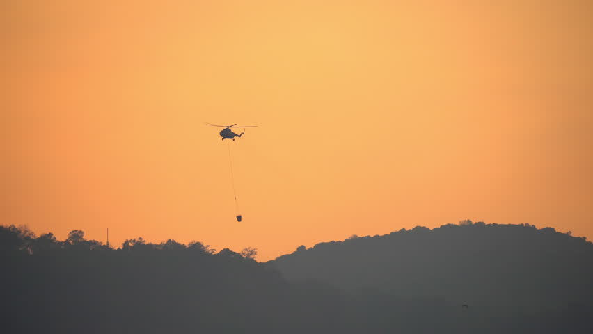 Fire fighting helicopter carry water bucket to put out a forest fire.
